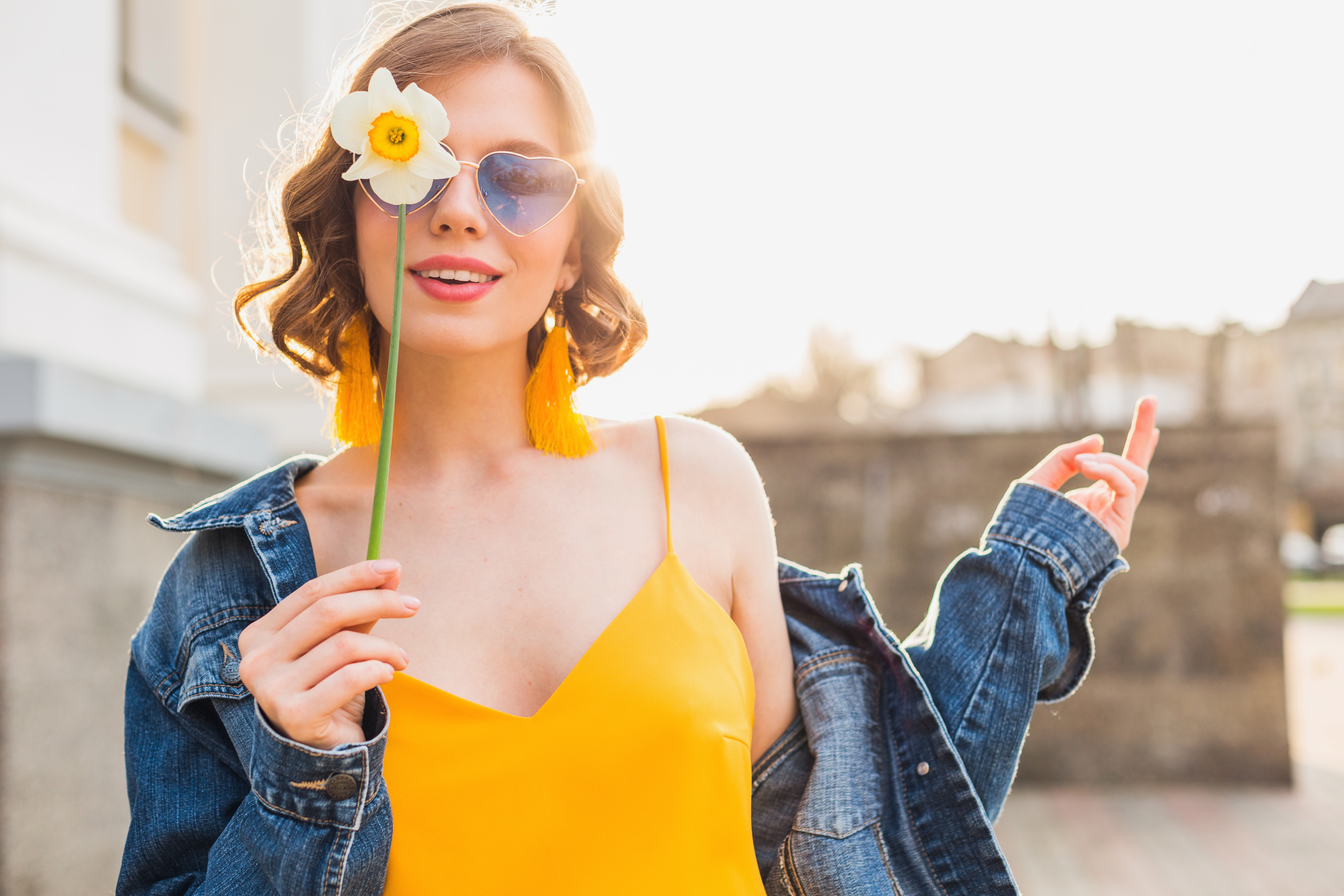 bright portrait of beautiful woman holding flower, yellow dress, denim jacket, hipster style, summer fashion trend, smile, trendy sunglasses