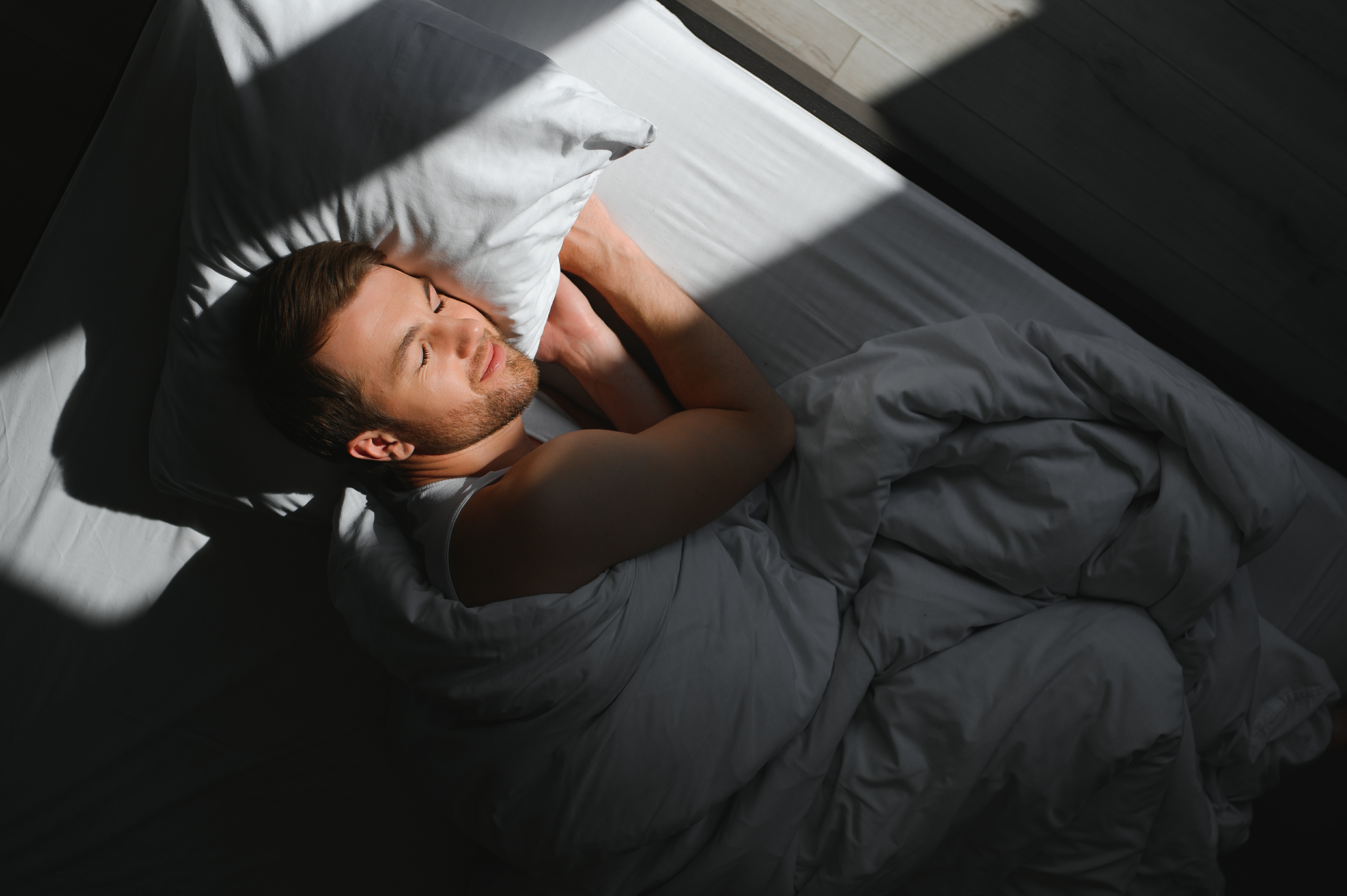 Handsome man sleeping under soft blanket in bed at home.