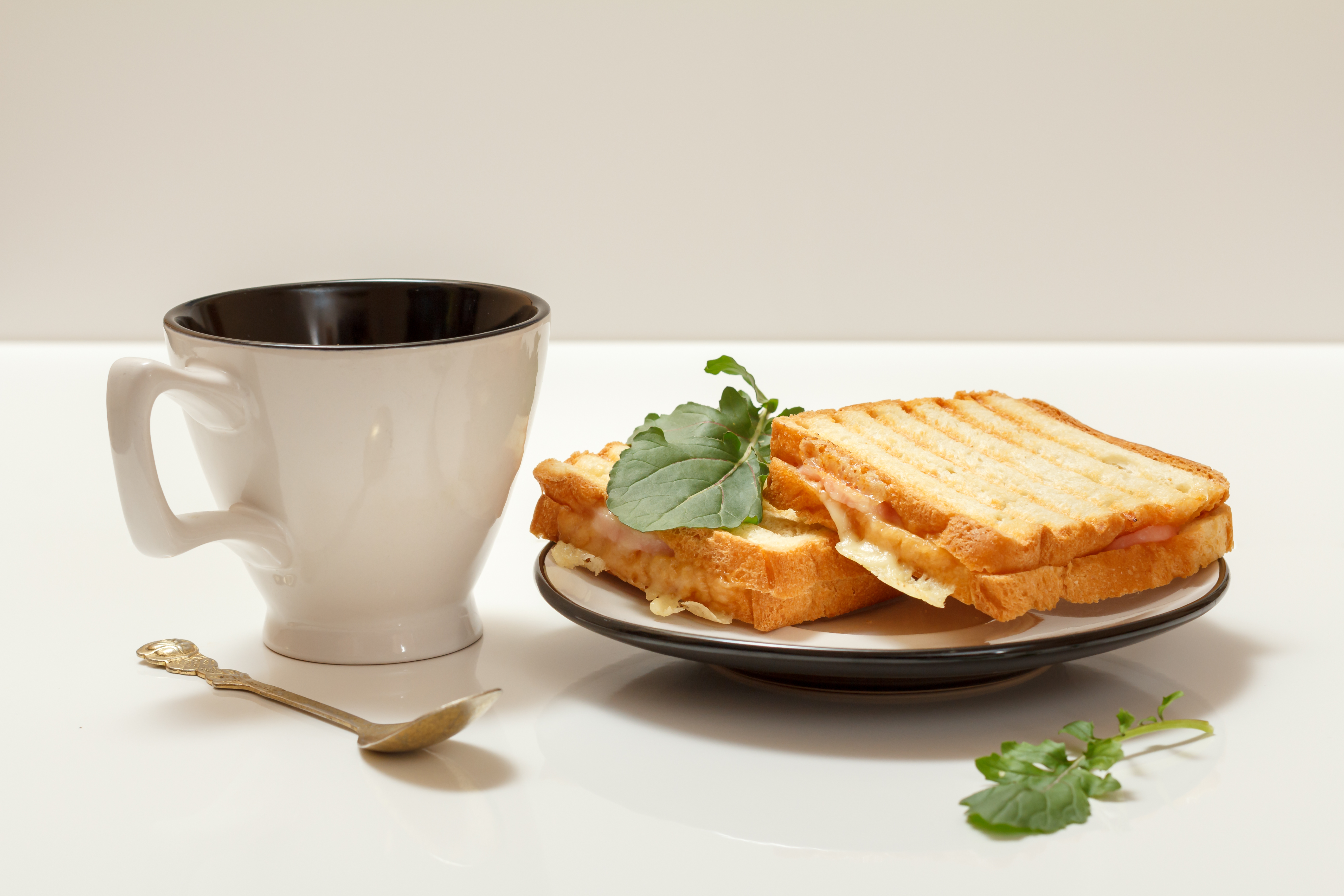 Homemade grilled cheese sandwiches for breakfast on a plate and a cup of coffee with a spoon.